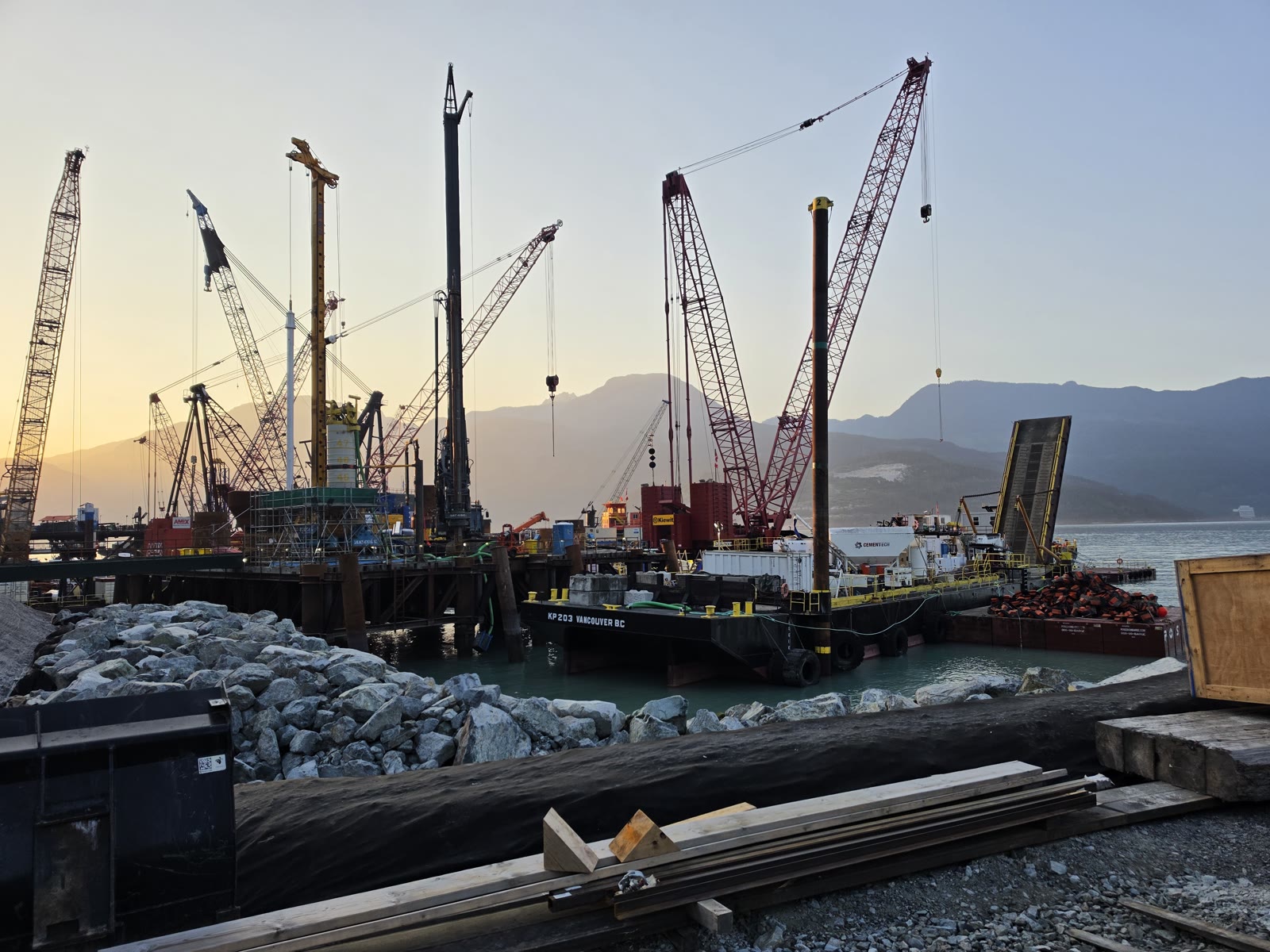 Barge-mounted concrete plant and cranes at dawn on a coastal inlet