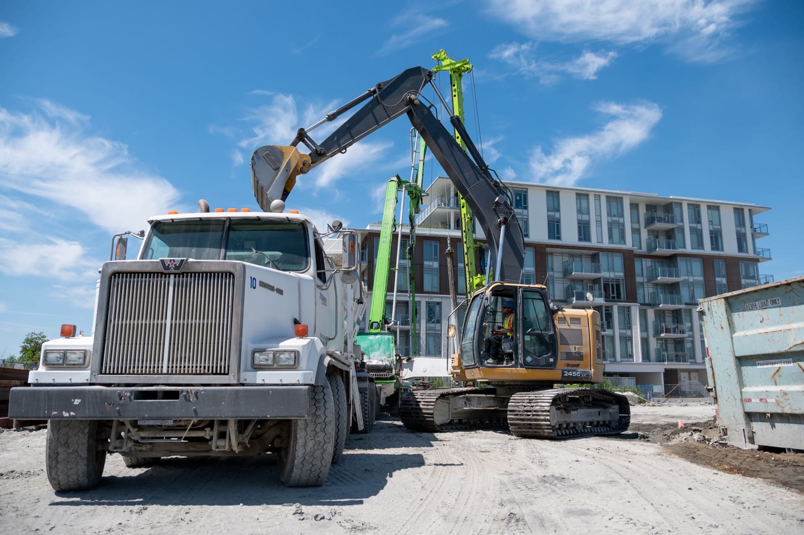 Volumetric mixer, excavator and drilling rig working beside a residential building