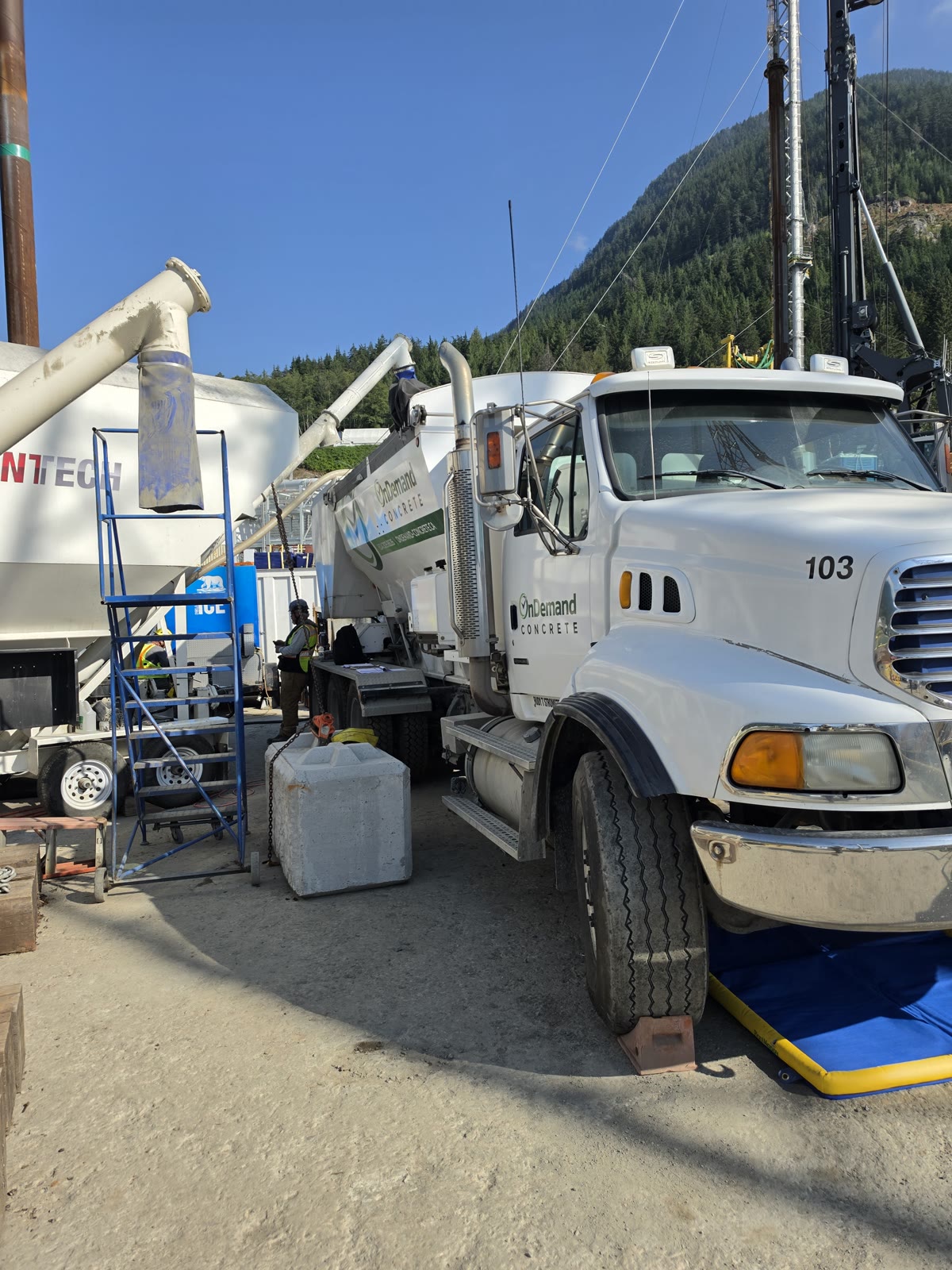 Volumetric mixer and cement silo set up on a barge below a forested mountain