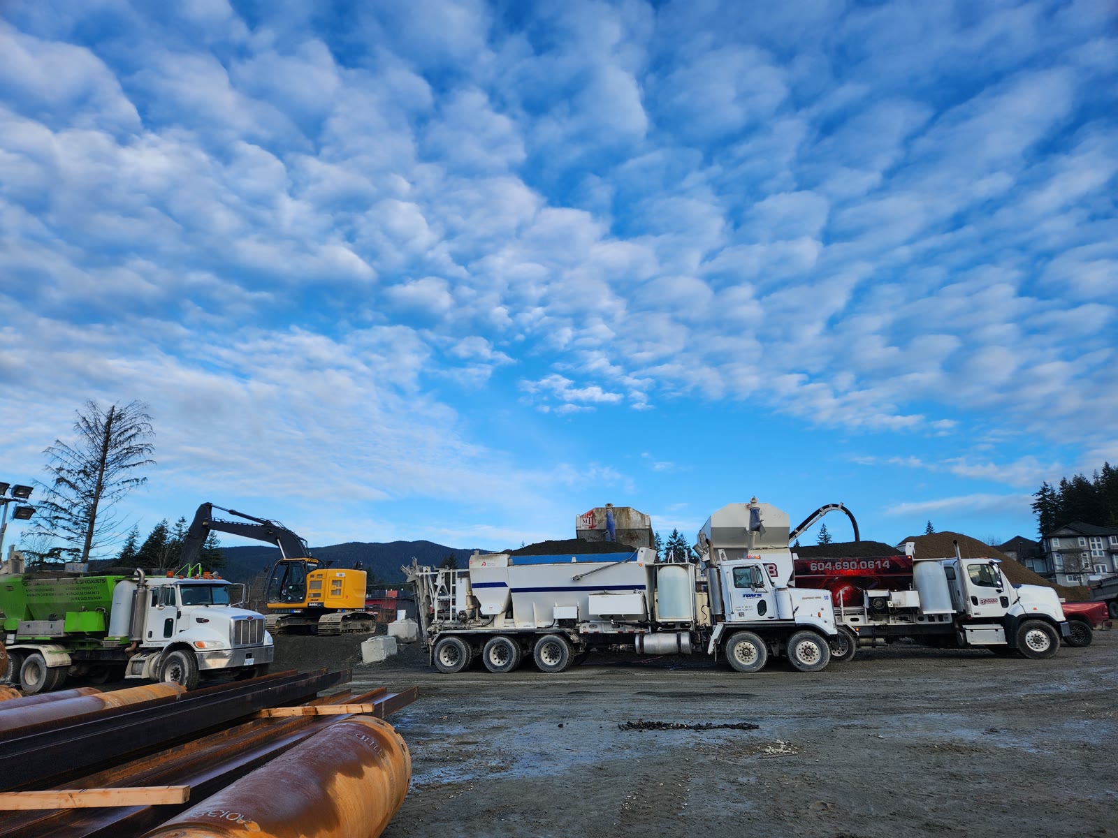 A line of volumetric concrete mixers parked in a yard under a wide morning sky