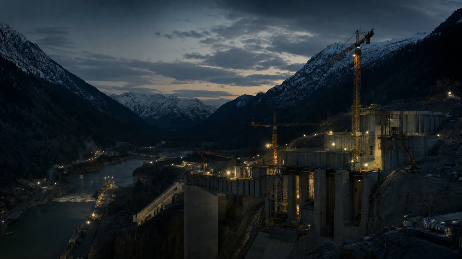 Large-scale heavy-civil infrastructure under construction in a British Columbia mountain valley at dusk