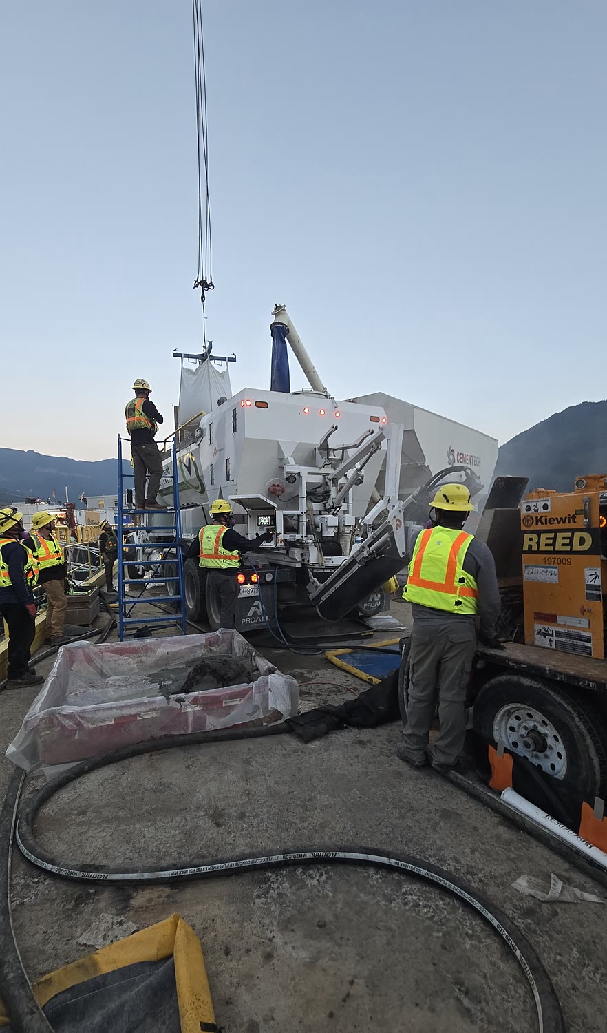 Sustainable Concrete crew operating a volumetric mixer with contained washout on a coastal industrial site at dusk