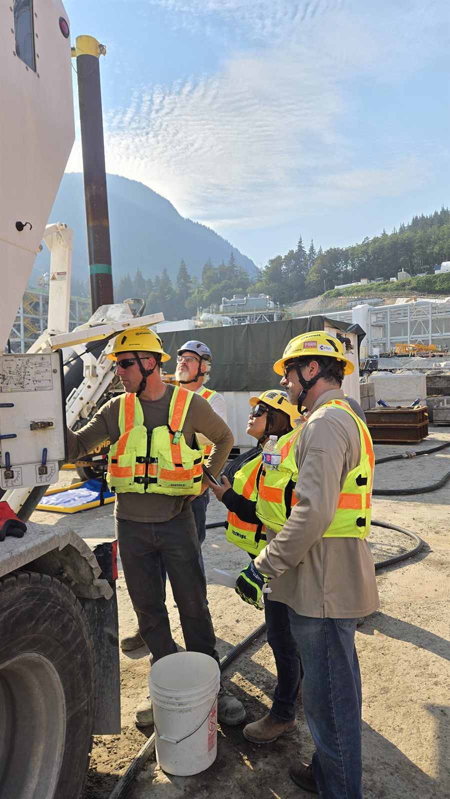Sustainable Concrete and Kiewit crew at the volumetric mixer on the Woodfibre LNG site, with the LNG plant and Howe Sound mountains behind